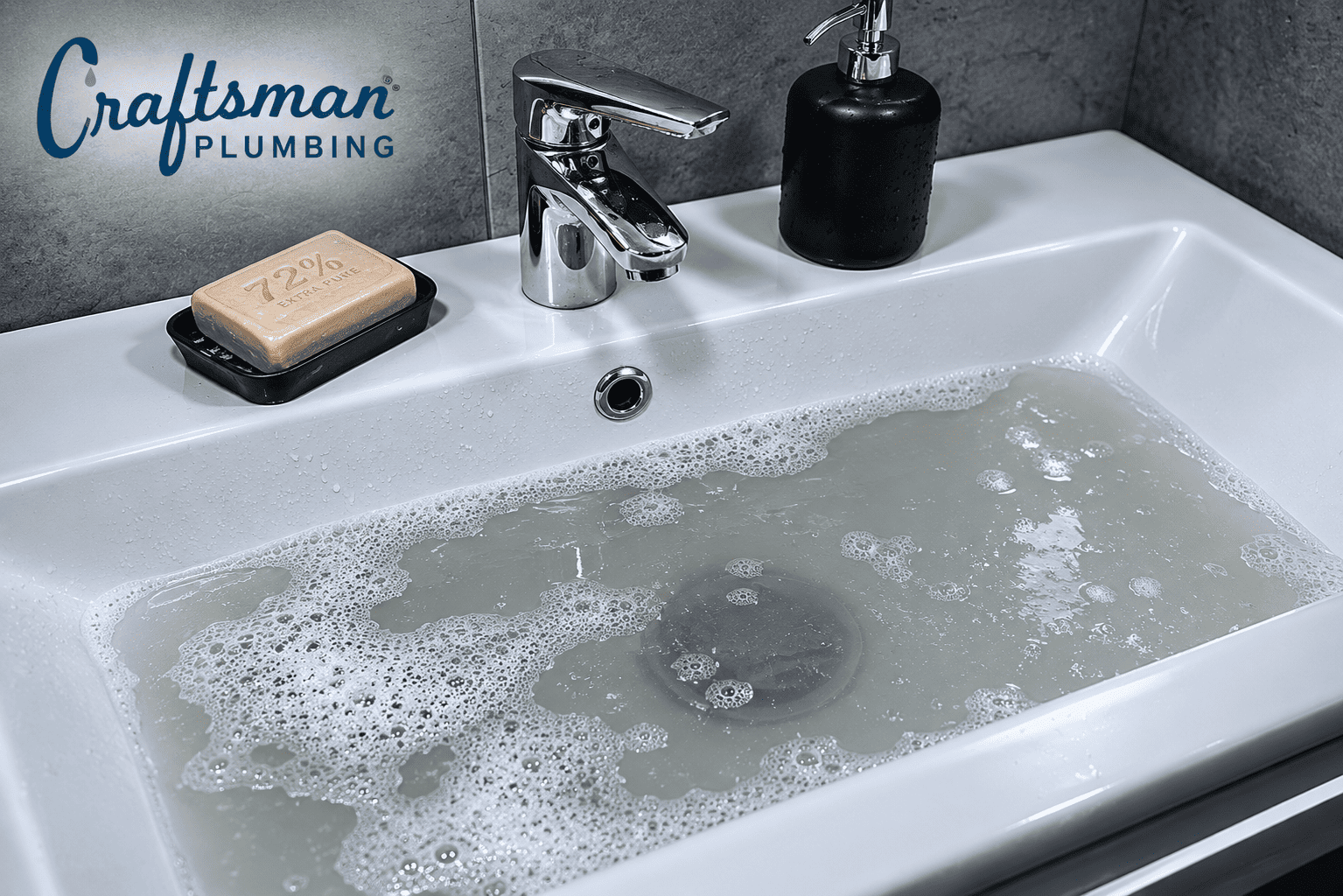 Bathroom sink filled with cloudy soapy water draining slowly, with the Craftsman Plumbing logo in the upper left corner.